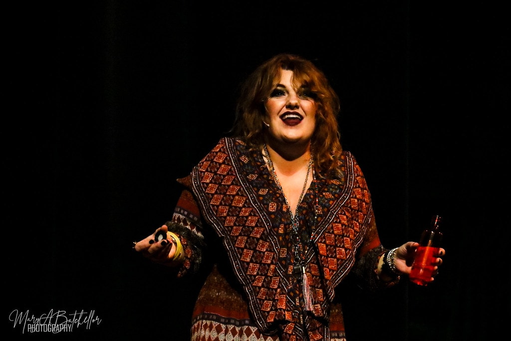 Annie — Miss Hannigan belts a solo with arms wide on the dark stage