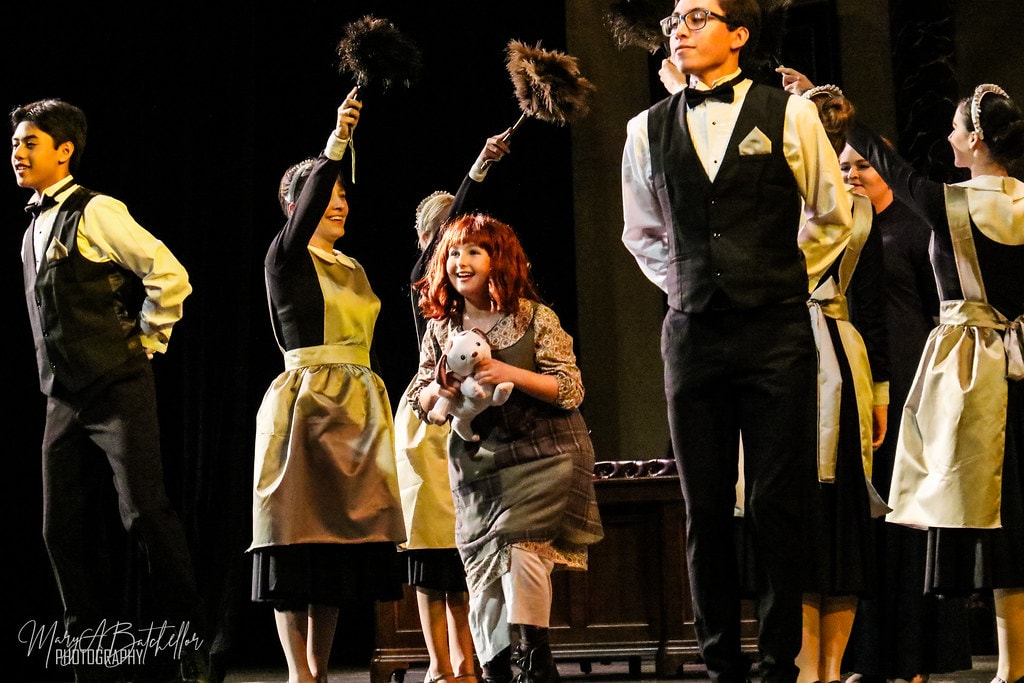 Annie — Annie laughs with delight as Warbucks mansion staff wave feather dusters around her