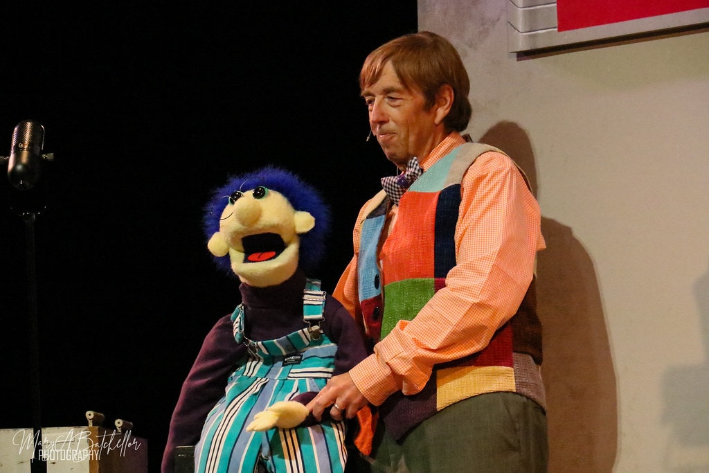 Annie — the ventriloquist holds his blue-haired puppet Sandy beside the vintage radio microphone