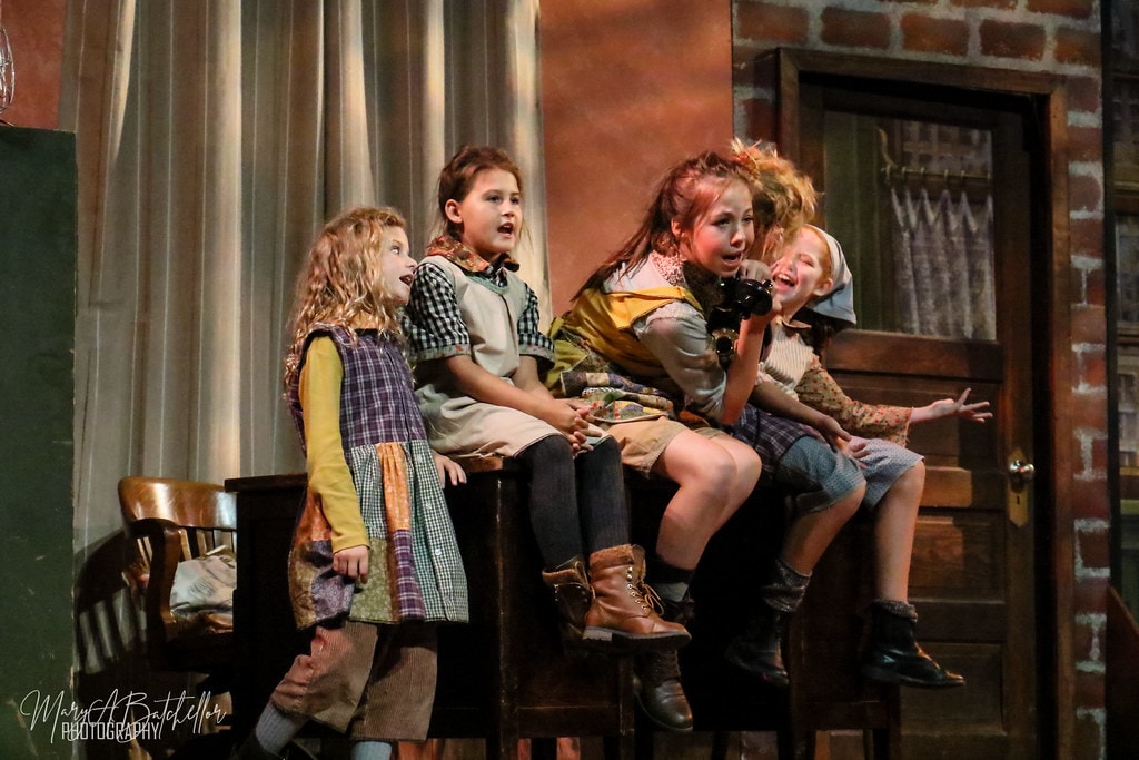 Annie — four orphan girls sit together on a wooden cabinet clutching a vintage telephone