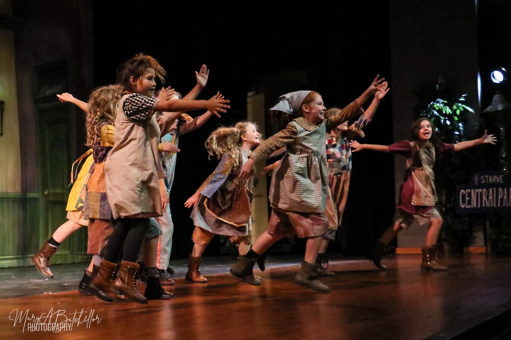 Annie — eight orphan girls leap with arms outstretched before the Central Park backdrop