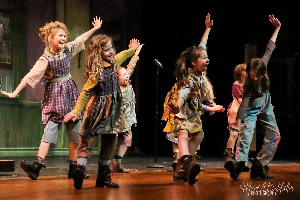Annie — six orphan girls skip and dance with arms raised before the Central Park backdrop