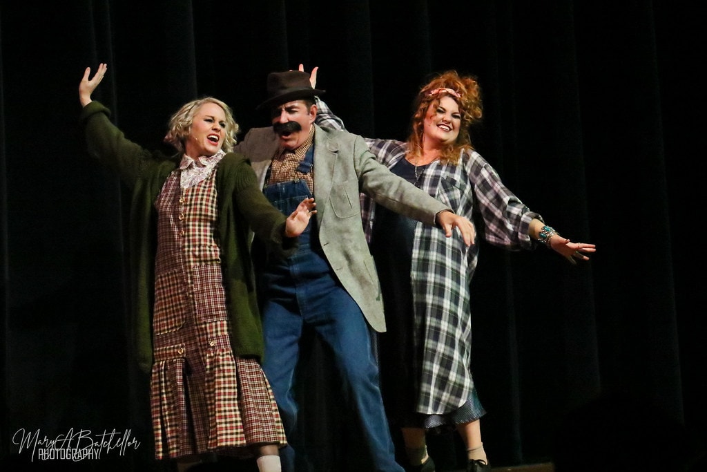 Annie — three adults in plaid and overalls period costumes sing together with arms wide