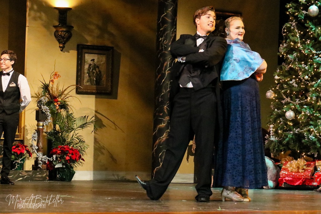 Annie — Oliver Warbucks and a woman in a blue gown pose back-to-back beside the Christmas tree