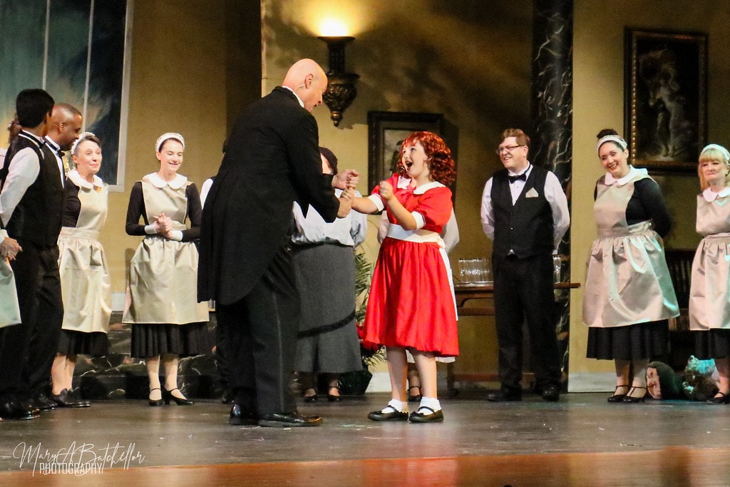 Annie — Oliver Warbucks dances with Annie in her red dress as the mansion staff cheers