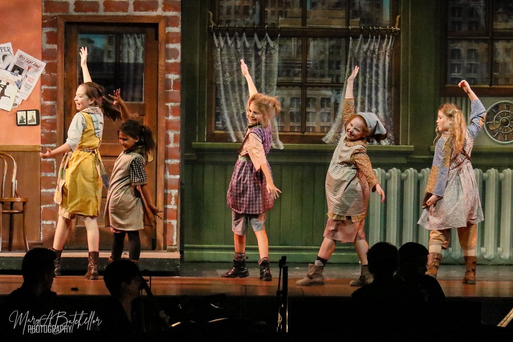Annie — five orphan girls dance with arms raised before the Warbucks apartment backdrop