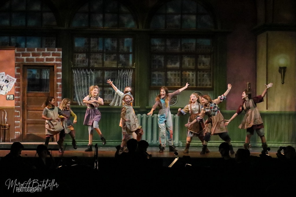 Annie — nine orphan girls leap and dance with arms wide before the full Warbucks apartment set
