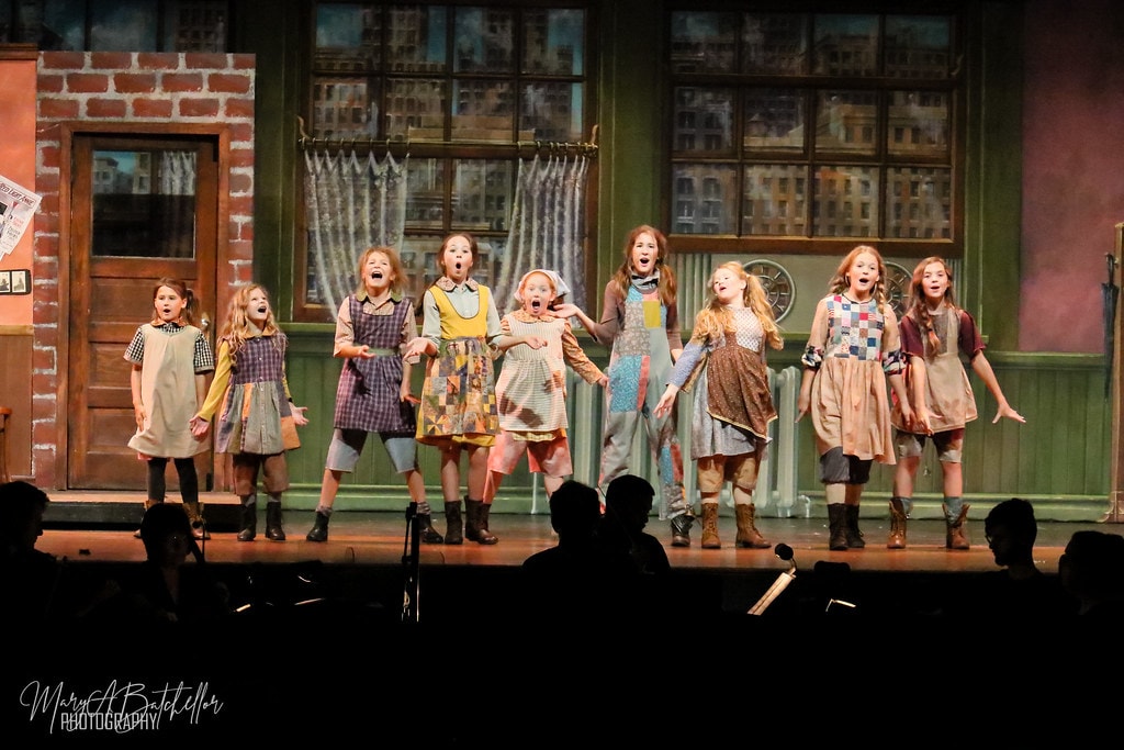 Annie — nine orphan girls sing together in a wide line before the Warbucks apartment set