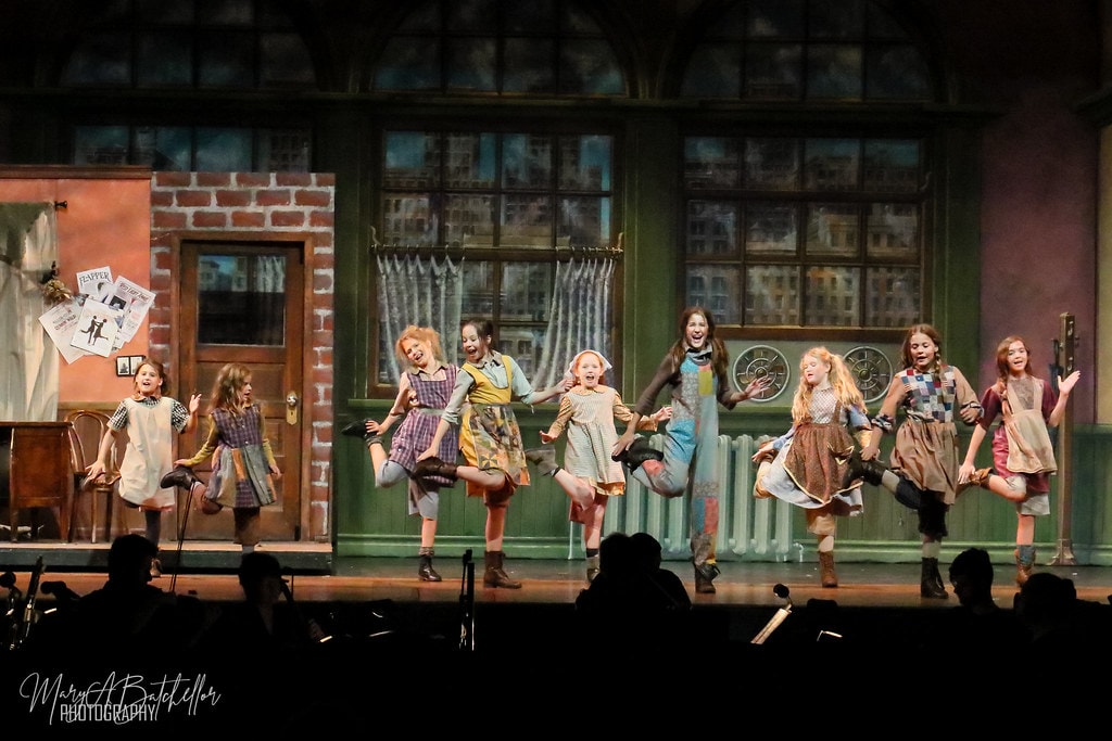 Annie — nine orphan girls kick their legs in a joyful chorus line before the orphanage set