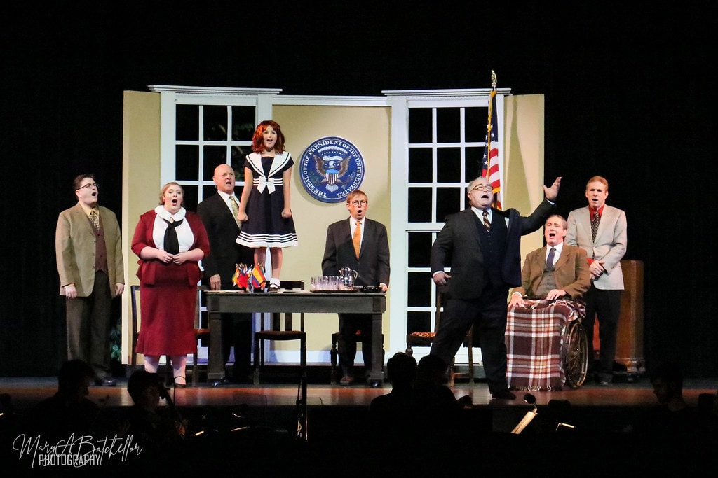 Annie — Annie in her navy sailor dress stands center stage before the Presidential Seal