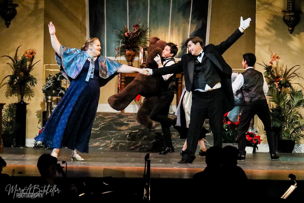Annie — a woman in a blue cape, a performer in a bear costume, and a man in a tuxedo dance together