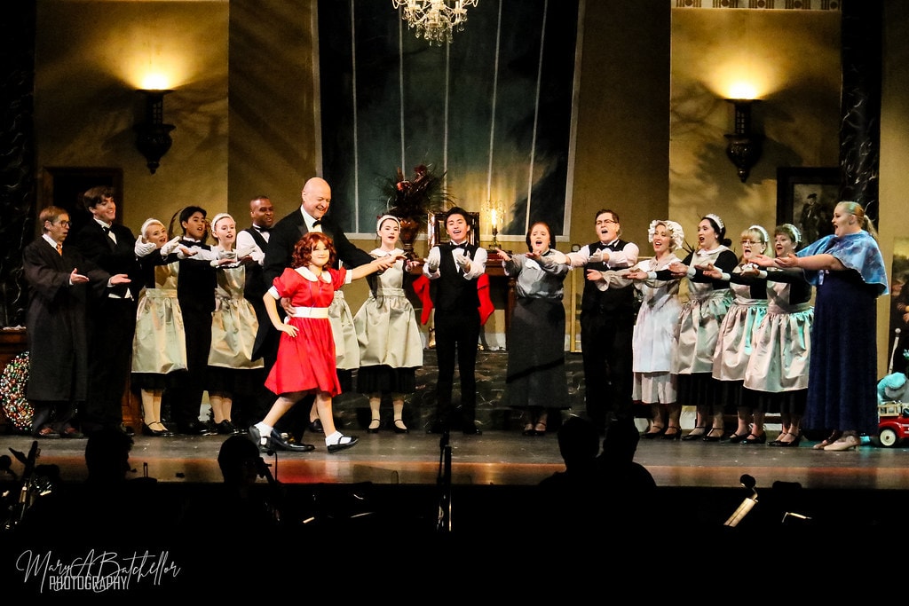 Annie — the full Warbucks mansion cast extends their arms toward Annie in a joyful ensemble number