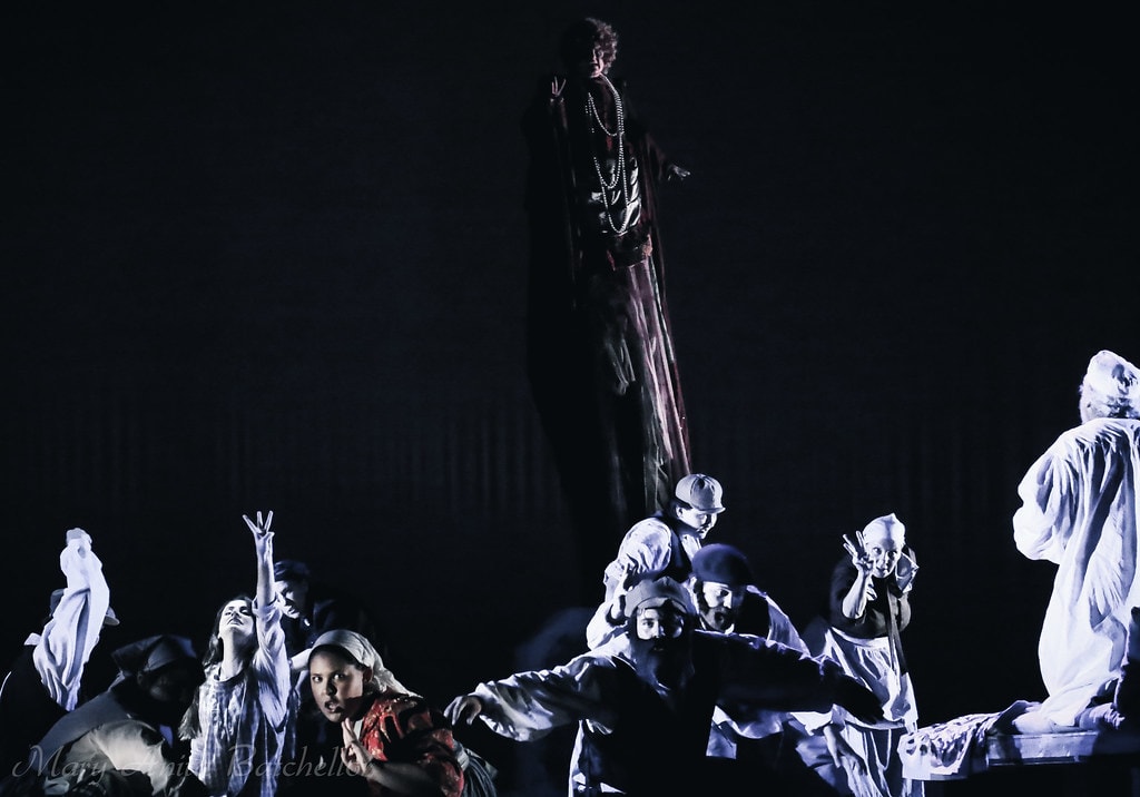 Fiddler on the Roof — a dark-robed figure stands elevated on a tall platform while the ensemble in white nightgowns reaches upward in the dramatic dream sequence