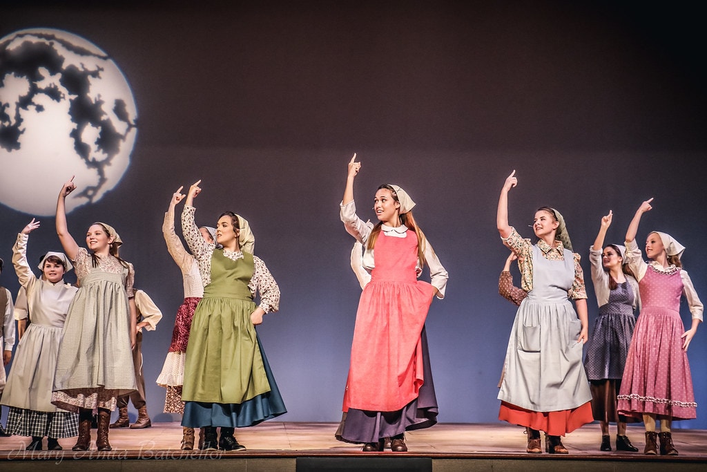 Fiddler on the Roof — eight young women in colorful aprons and headscarves point upward joyfully in the Matchmaker number