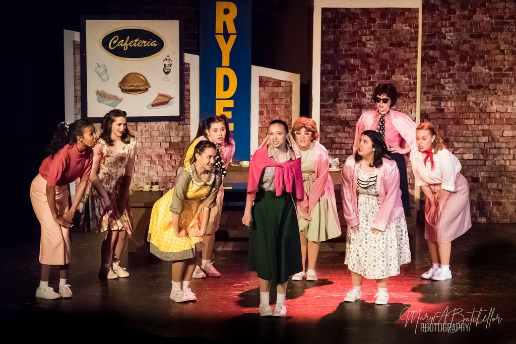 Grease — Sandy center stage at Rydell cafeteria with full cast