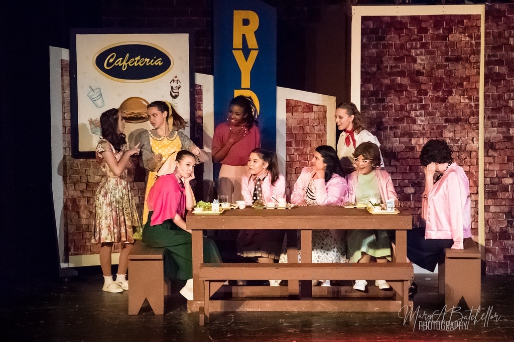 Grease — Pink Ladies seated at cafeteria table with Sandy and Frenchie