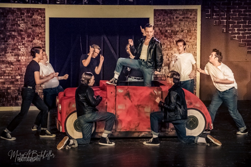 Grease — Danny standing on red car prop with T-Birds surrounding him