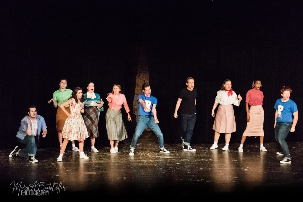 Grease — Pink Ladies and cast surrounding Sandy at Rydell cafeteria