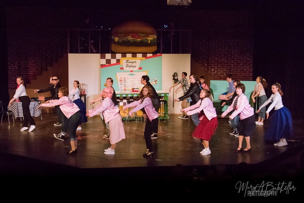 Grease — full cast kicking and dancing at Burger Palace set