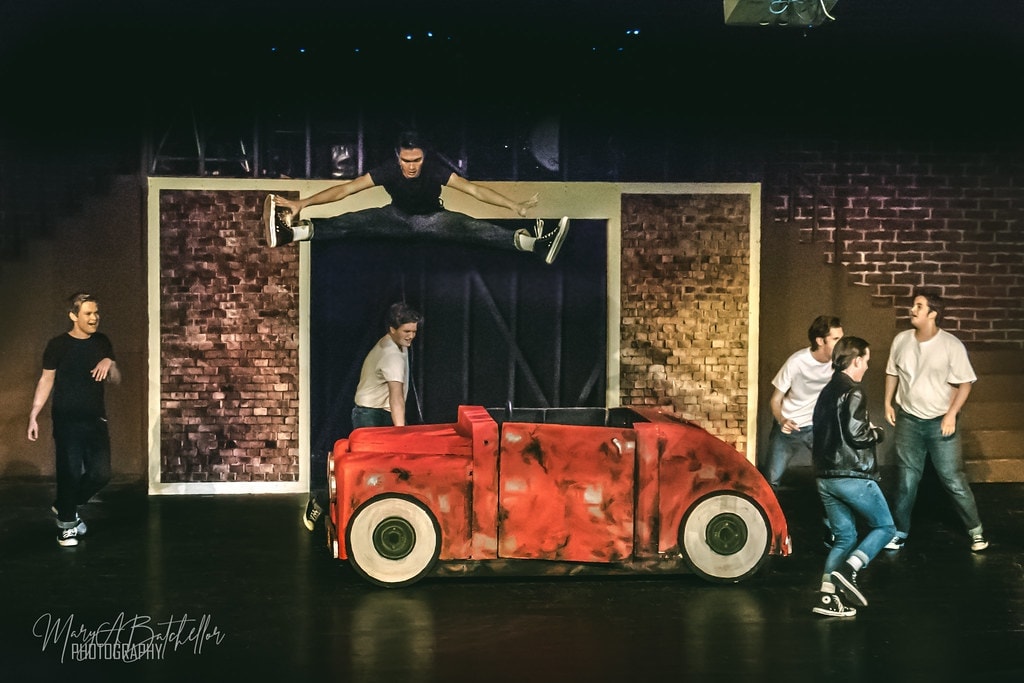 Grease — Danny leaping in a split over the red car prop