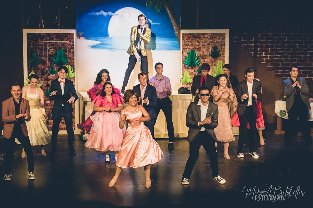 Grease — full cast at beach party with Teen Angel elevated on platform