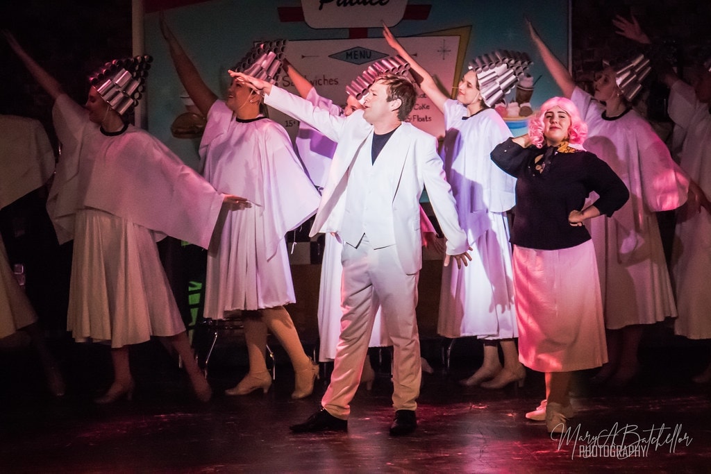 Grease — Teen Angel in white suit arms wide with full angel ensemble