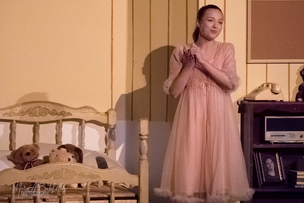 Grease — Sandy in pink nightgown standing by her bed with teddy bears