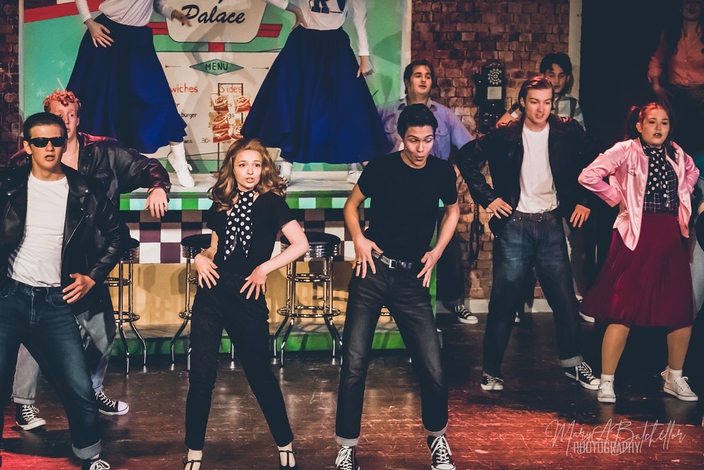 Grease — Sandy in polka-dot blouse and Danny facing off in dance challenge