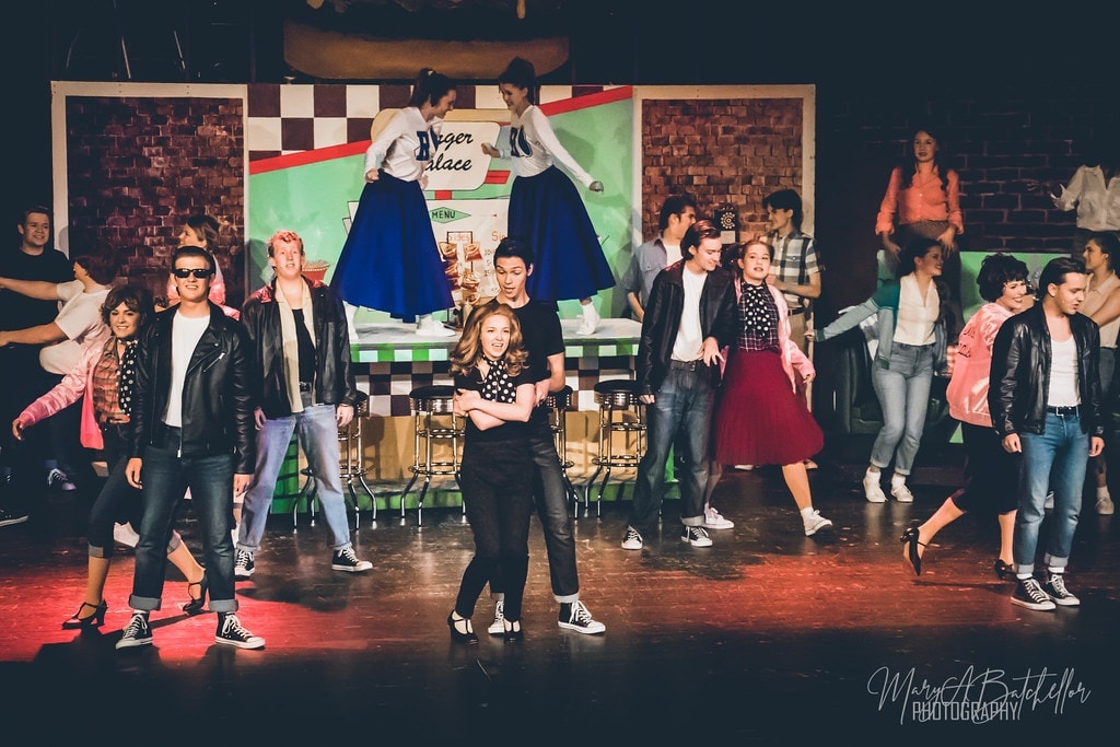 Grease — full cast mid-dance at Burger Palace with cheerleaders elevated