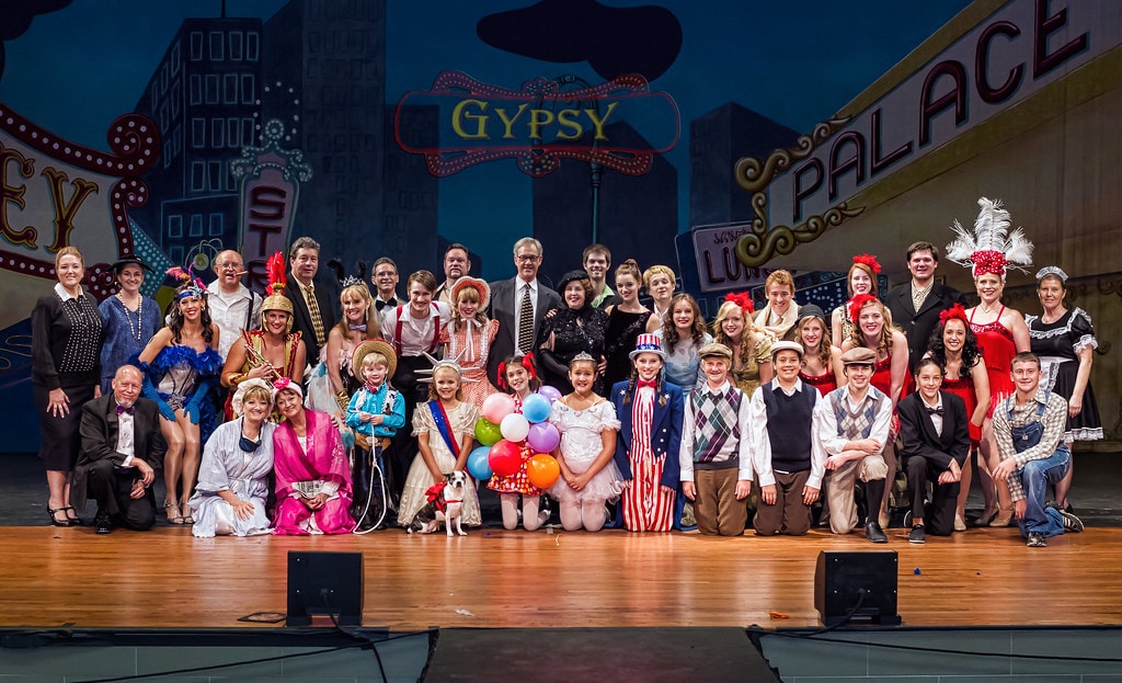 Gypsy — the full cast of over 40 performers poses for a company photo on stage before the colorful Gypsy Palace backdrop with the show title in neon lights
