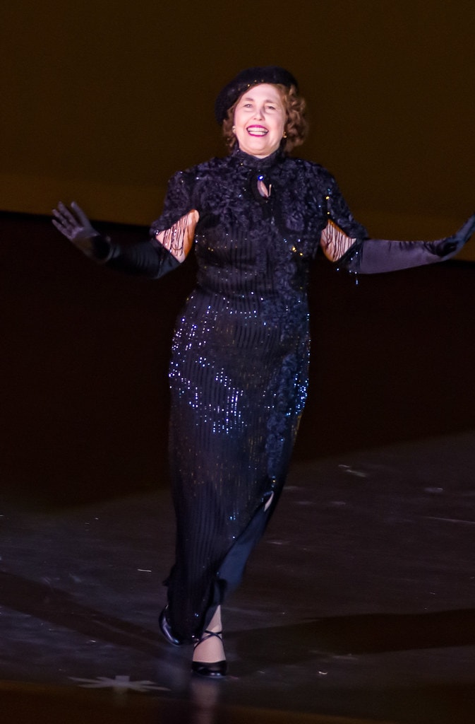 Gypsy — Rose in a sparkling black beaded gown and beret performs her solo with arms outstretched and a joyful expression against a warm amber-lit stage