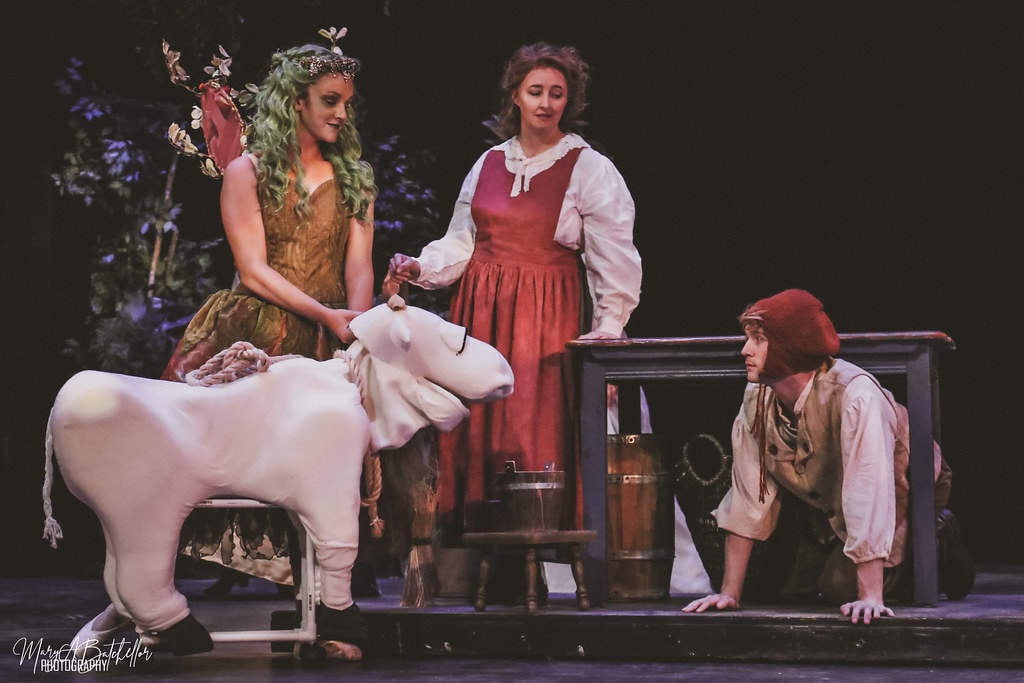 Into the Woods — the Witch with green hair and fairy wings hands Jack's cow to the Baker's Wife as Jack kneels nearby