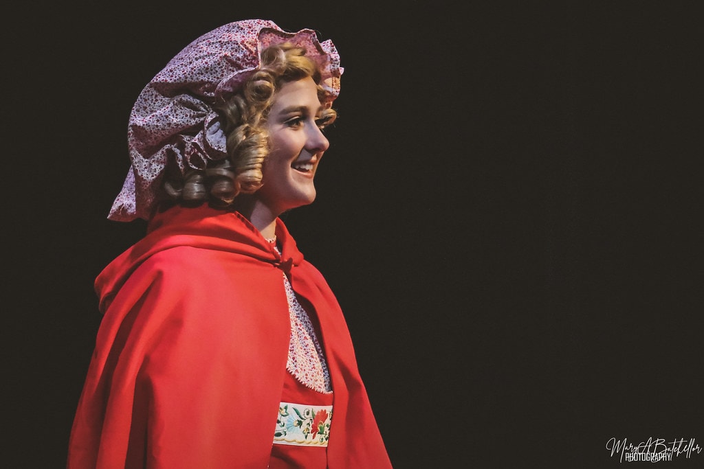 Into the Woods — Little Red Riding Hood in her red cape and floral bonnet smiling in profile