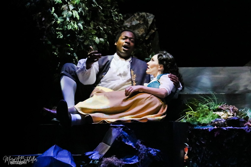 Into the Woods — Rapunzel's Prince and Cinderella sit together on a forest bench in an intimate scene