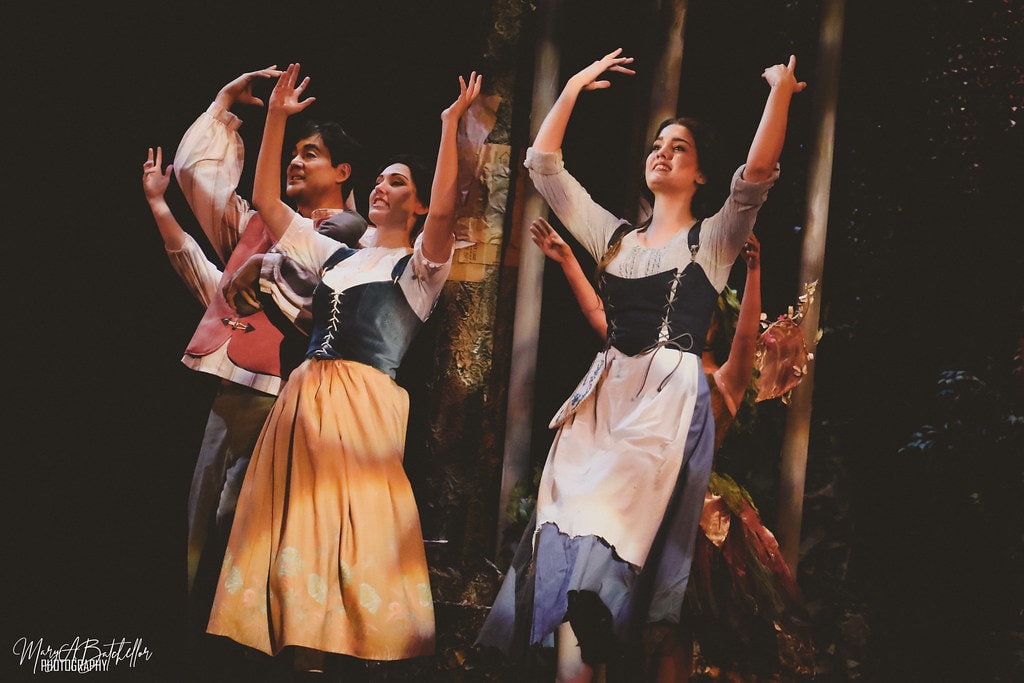Into the Woods — the Baker, Baker's Wife, and Cinderella raise their arms in the enchanted forest set
