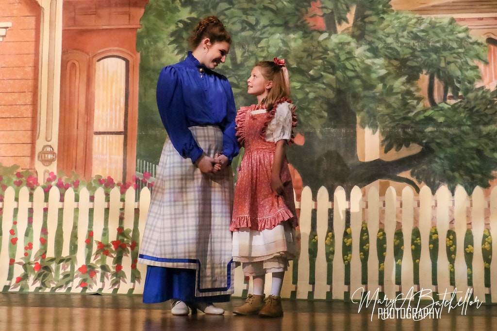 The Music Man — Marian holds hands with Amaryllis before the white picket fence backdrop