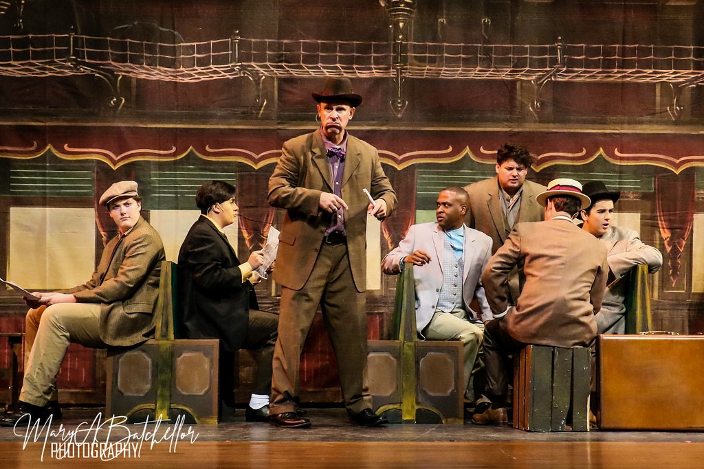 The Music Man — seven men in period suits in the train car