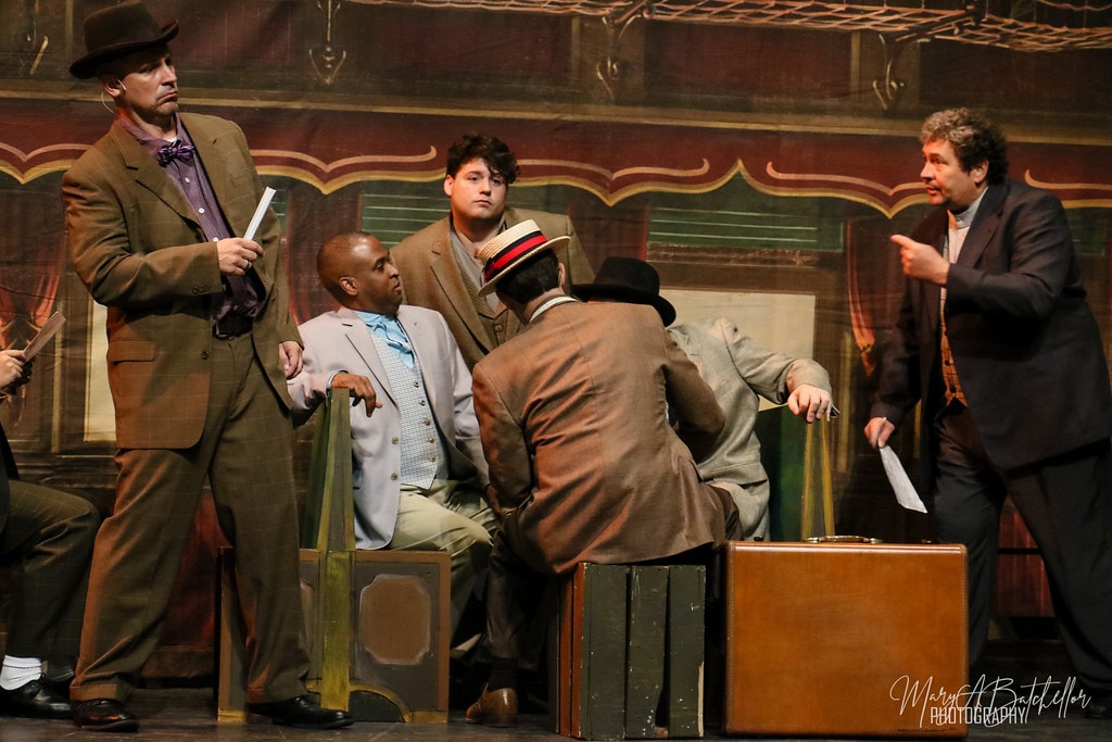 The Music Man — Harold Hill gestures to a man in a dark suit in the train car