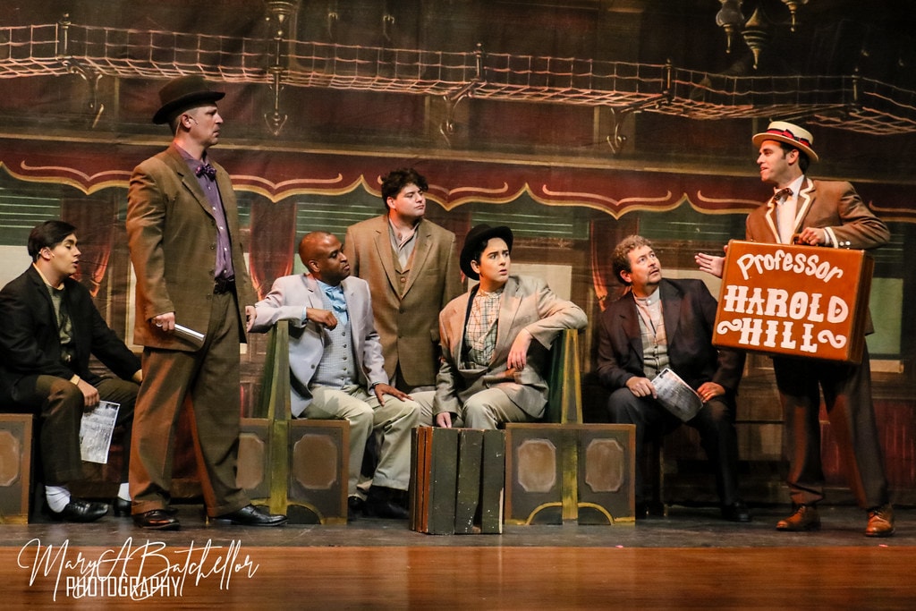 The Music Man — Harold Hill with his suitcase sign as six men in suits look on