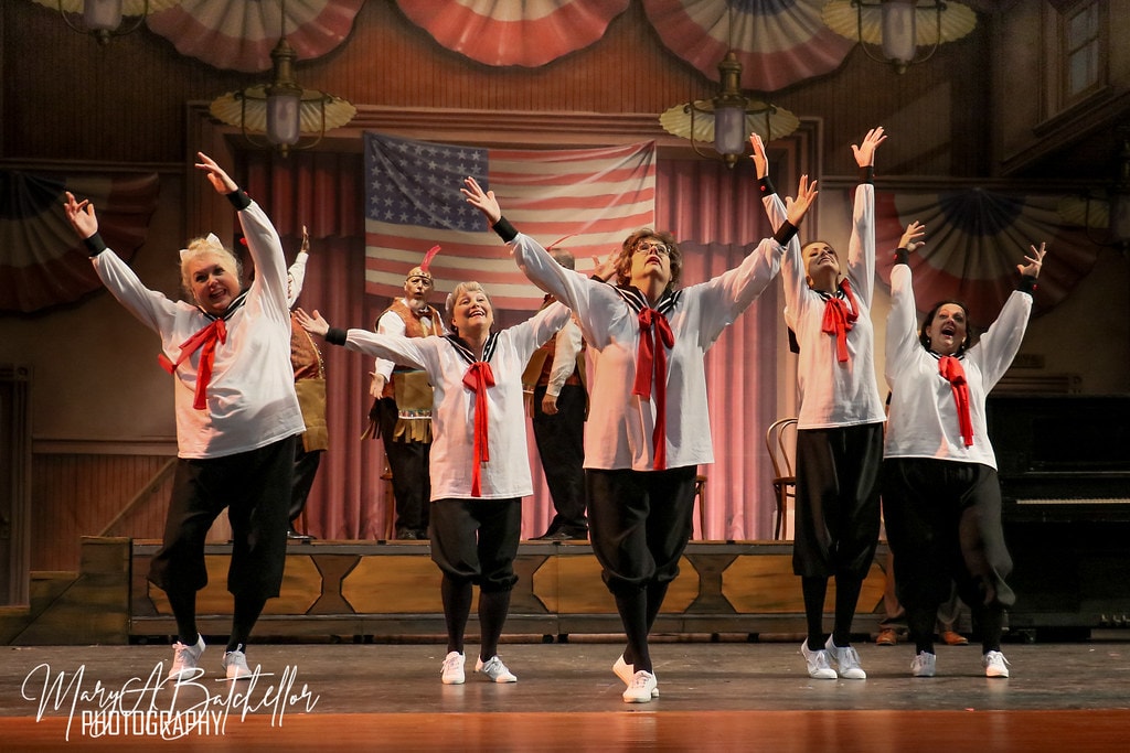 The Music Man — five women in white sailor tops with red ties raise their arms