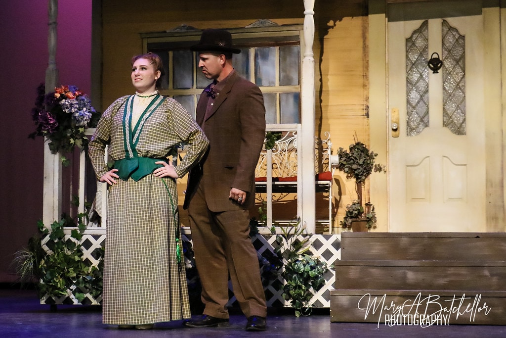 The Music Man — Marian in a plaid dress stands with hands on hips as Harold Hill looks on