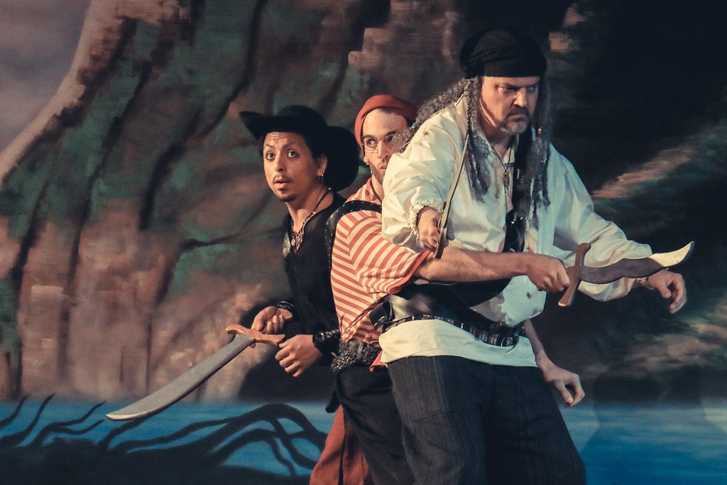 Peter Pan — three pirates with cutlasses crouch menacingly before the Neverland rock backdrop