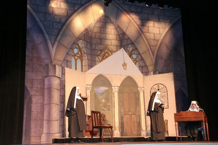 The Sound of Music — three nuns in black habits stand in the stone-arched convent chapel set with gothic windows and a hanging lantern