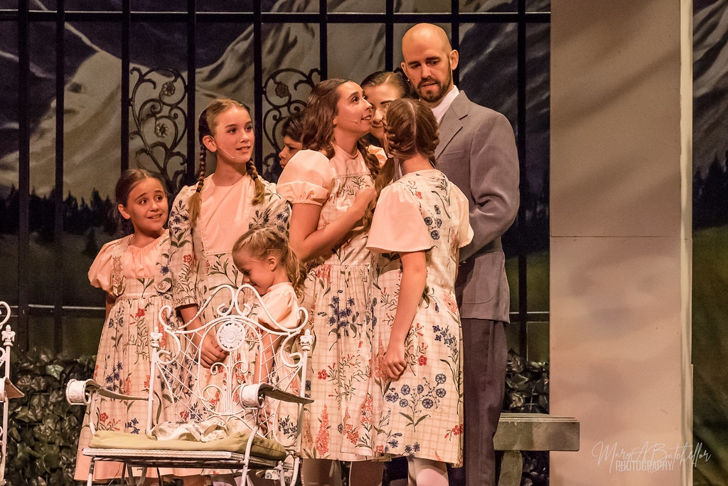 The Sound of Music — Maria in pink dirndl and Liesl in peach dress on the sofa