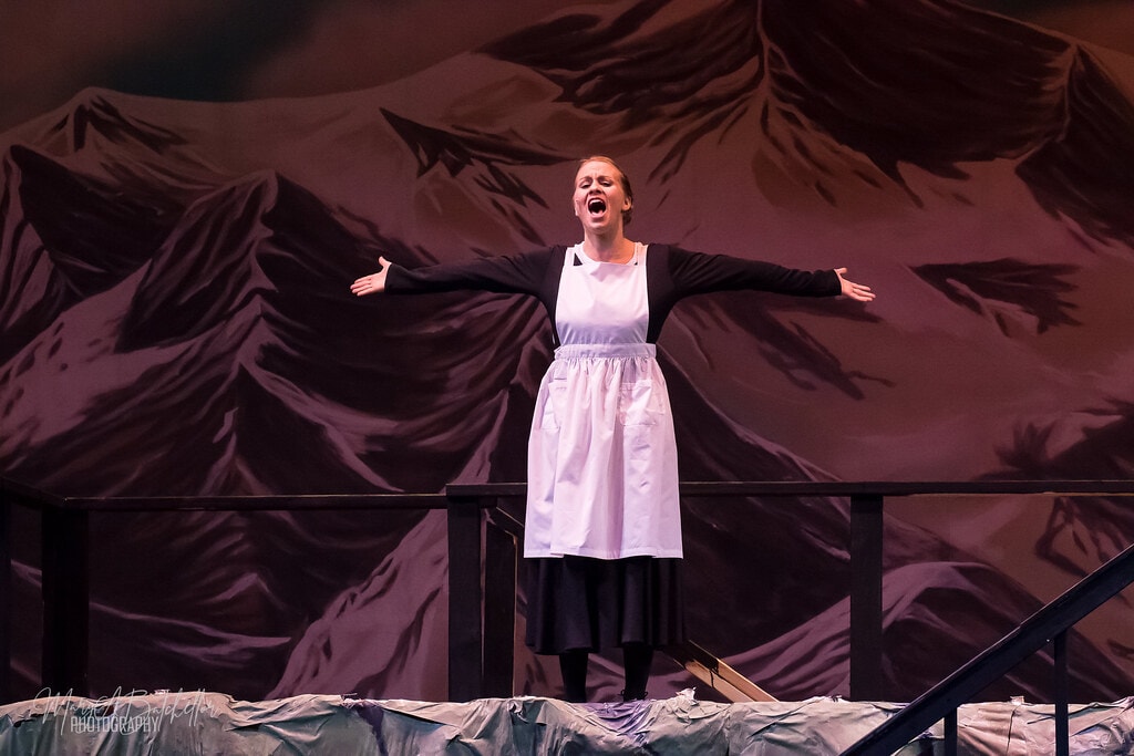 The Sound of Music — Maria in white apron singing before Alpine mountain backdrop
