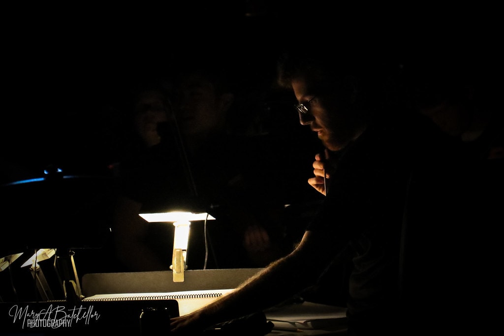 Thoroughly Modern Millie — a musician reads sheet music by a small lamp in the darkened orchestra pit