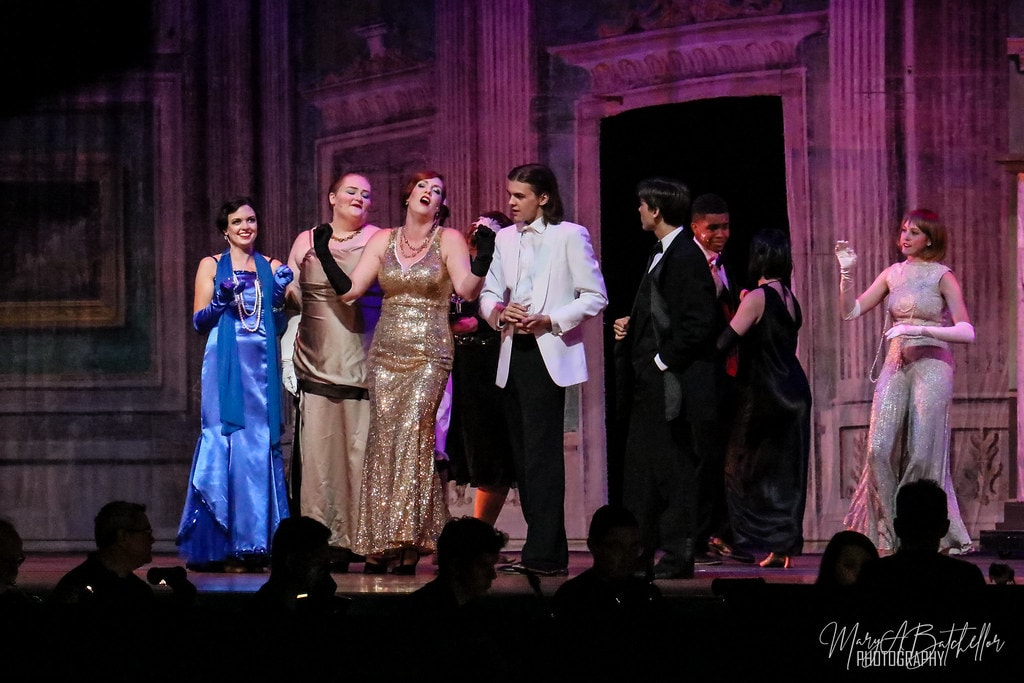 Thoroughly Modern Millie — the full cast in 1920s evening wear performs a wide ensemble number before the ornate ballroom backdrop