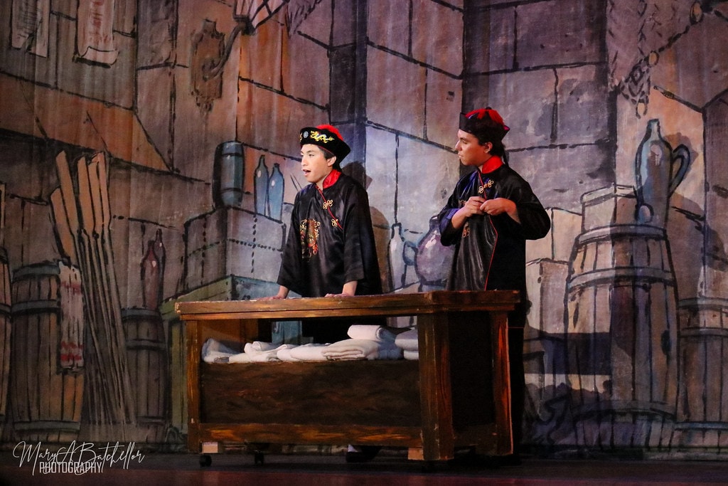 Thoroughly Modern Millie — two young men in black Chinese robes stand at a wooden laundry table