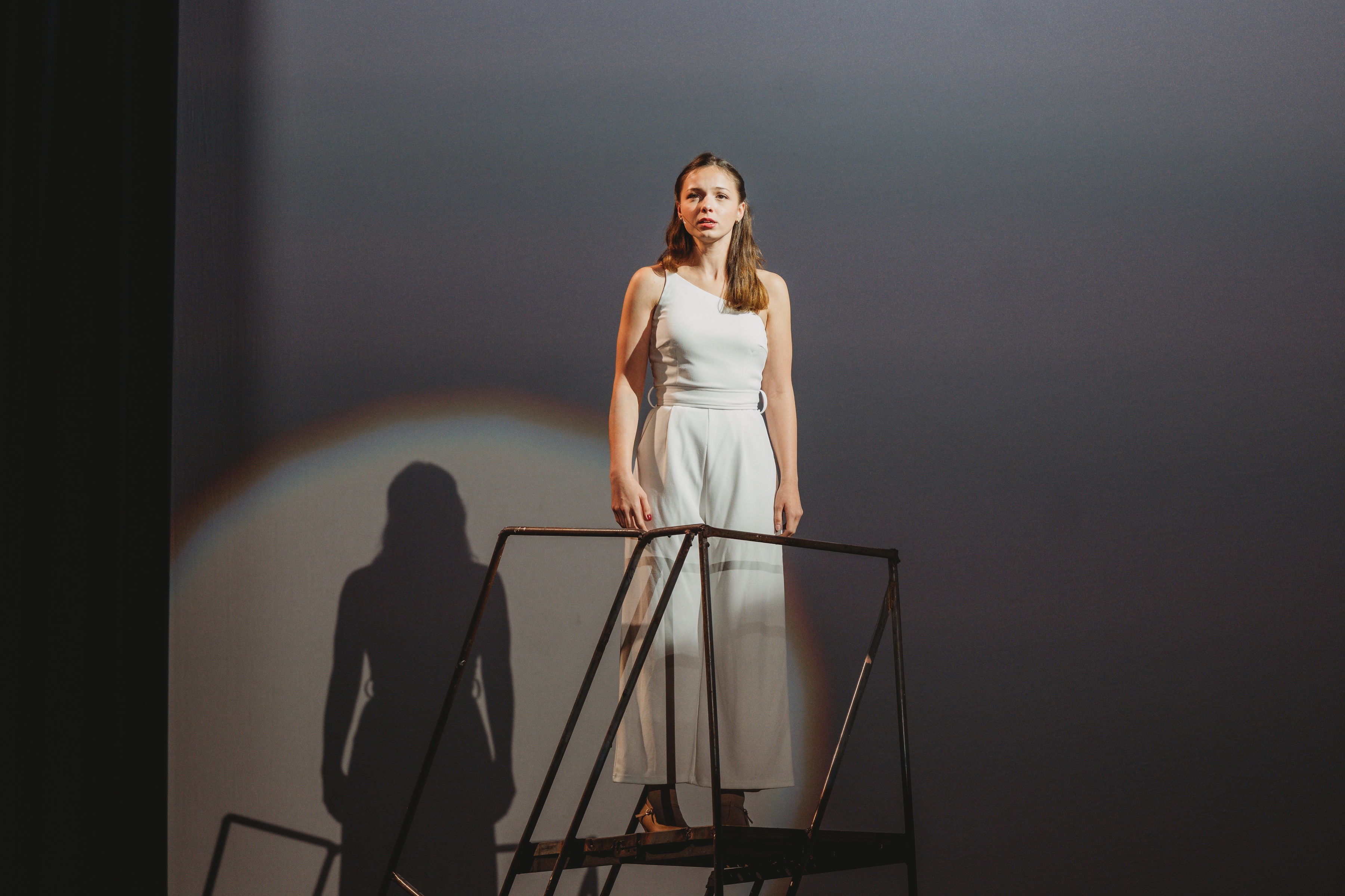 West Side Story 2026 - performer in white standing on scaffold with dramatic shadow