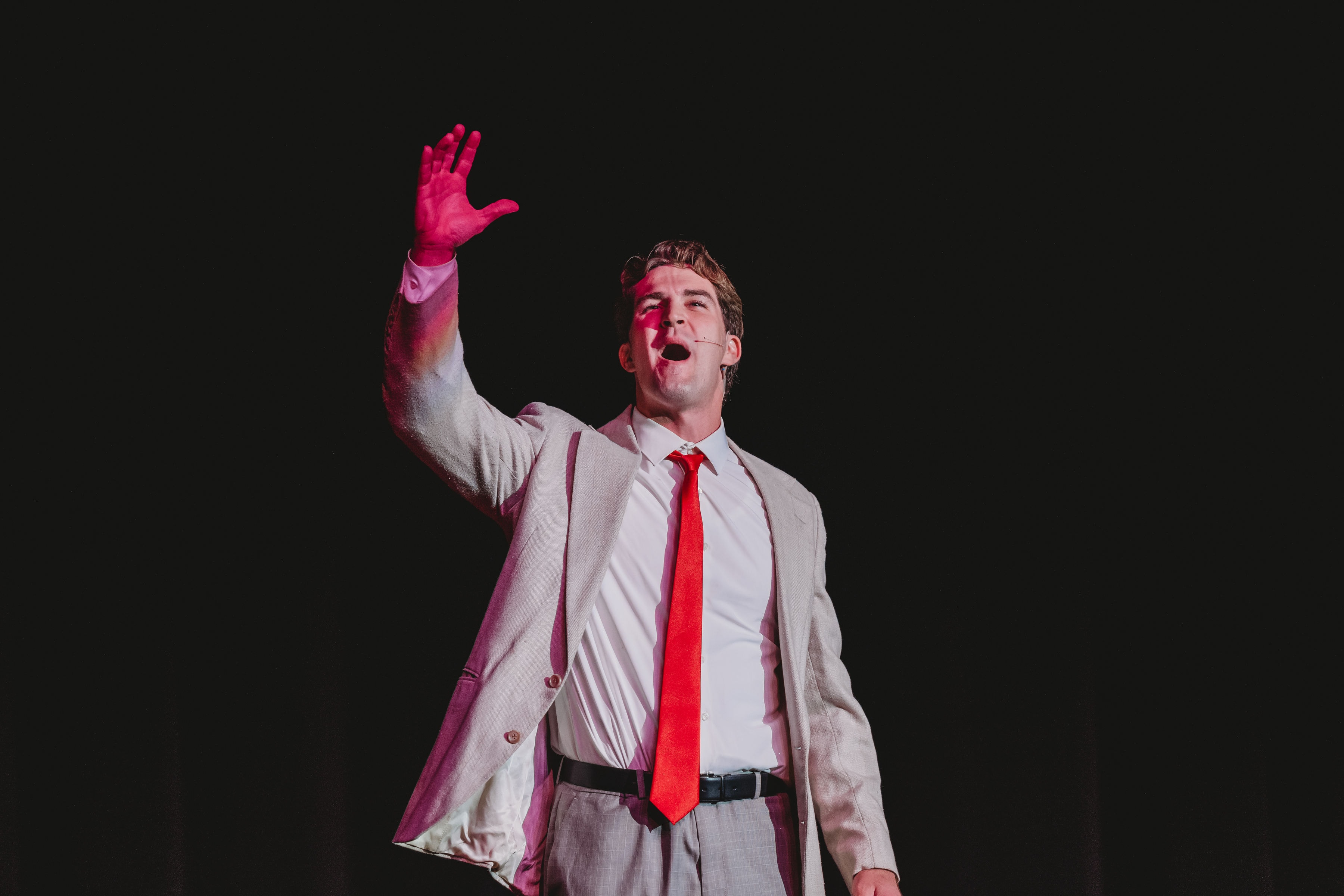 West Side Story 2026 - Tony singing solo with arm raised under dramatic pink spotlight